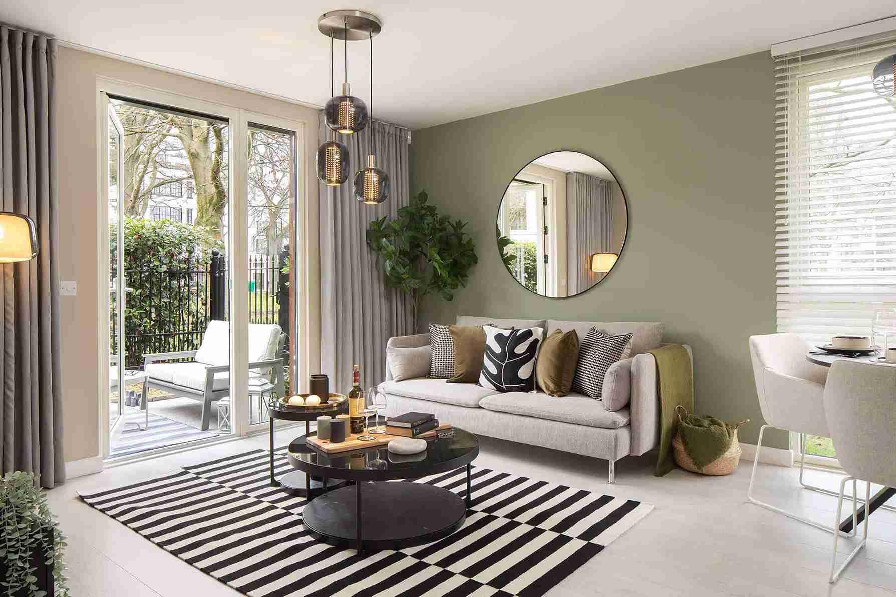 A living room in Hayes Village Homes with green walls and a black and white rug.