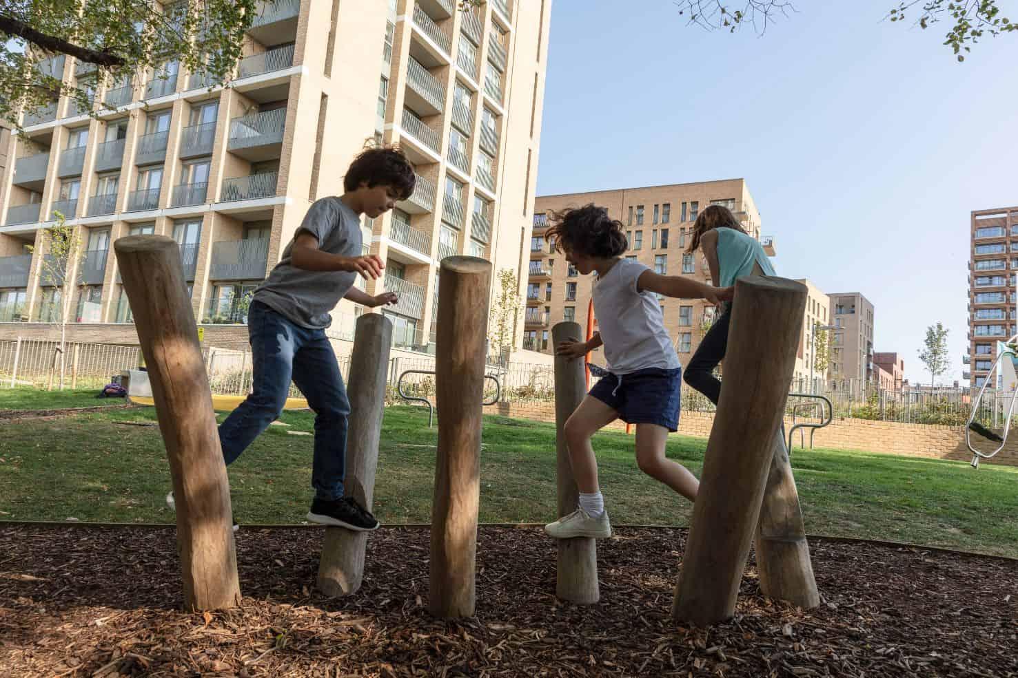 A group of children playing on wooden logs in a park in London